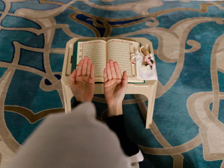 Voyageur musulman assis sur un tapis, mains levées en invocation, dans un paysage désertique.