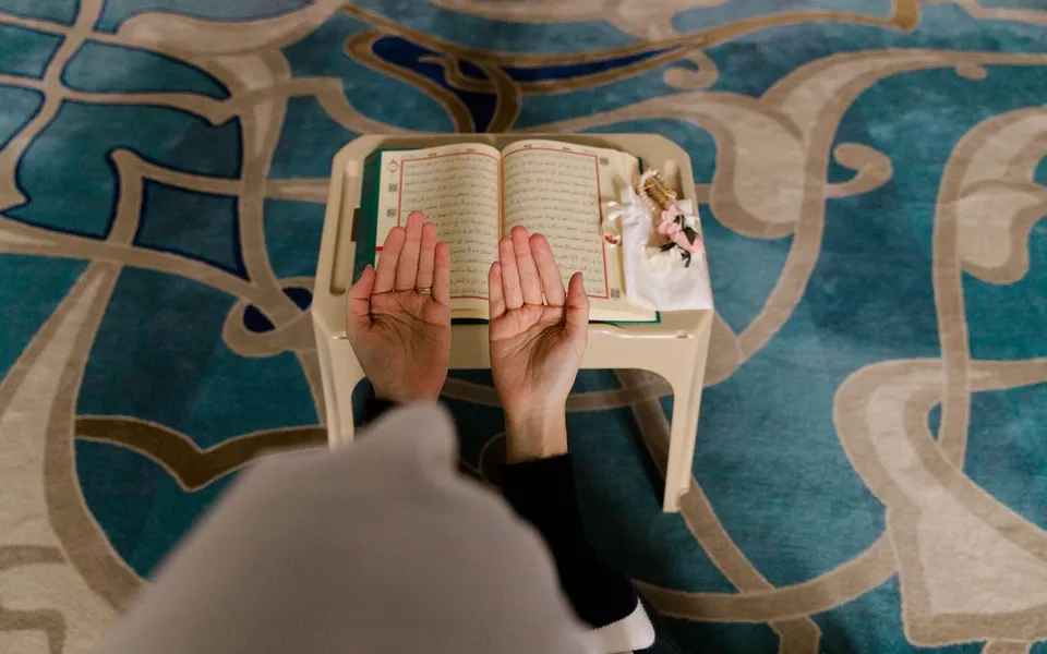 Voyageur musulman assis sur un tapis, mains levées en invocation, dans un paysage désertique.
